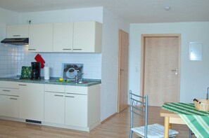 A compact kitchen with white cabinets, a sink, and a small dining area with a table and chair.