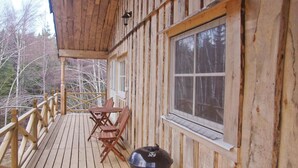 Eine Holzterrasse mit Tisch und Stühlen, einem Grill und einem großen Fenster mit Blick auf einen Wald.