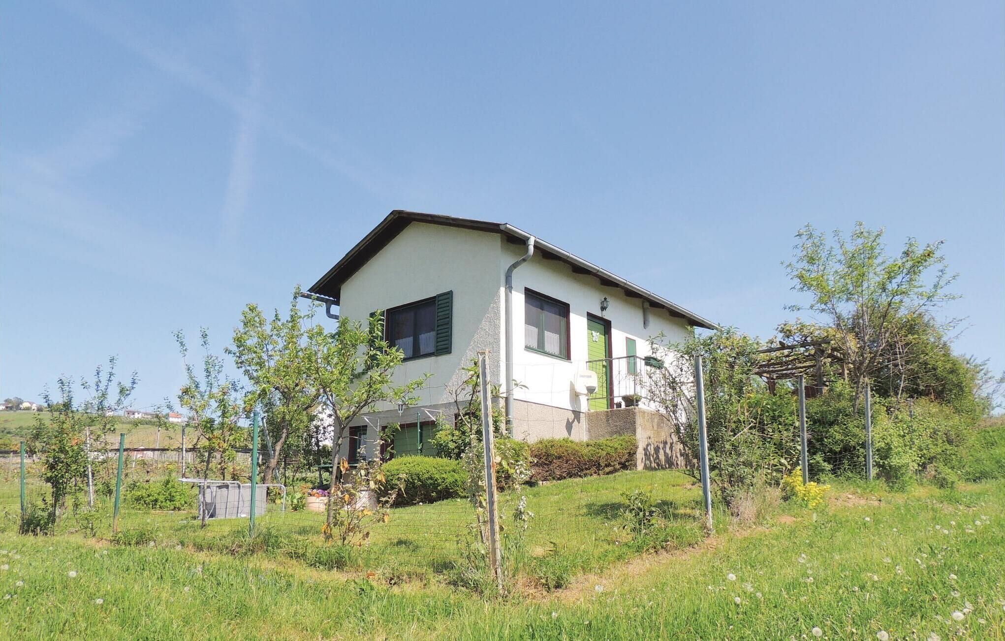 A two-story house with a sloped roof, a front porch, and a garden with young trees and shrubs.
