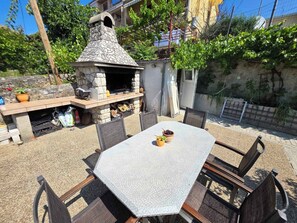 Patio esterno con zona barbecue in pietra, un tavolo e sedie.