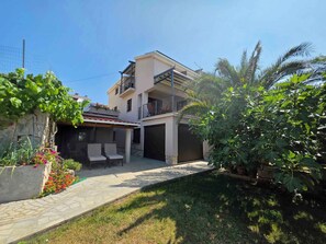 A two-story residential building with a covered patio area, outdoor seating, and lush greenery. - Holiday apartment with garden and air conditioning (Crikvenica)