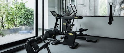 A gym with exercise equipment, large windows, and a view of greenery outside.