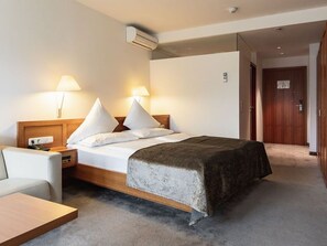 A hotel room with a bed, bedside lamps, a nightstand, a desk, and a door. - Family Suite - Hotel Goldenes Schiff (Bad Ischl)
