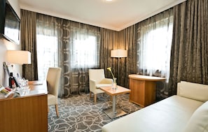 Ein Hotelzimmer mit Bett, Schreibtisch, Stuhl, einem kleinen Tisch mit Vase und zwei Lampen.