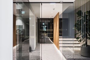 A modern hotel lobby with a glass door entrance, a wooden staircase, and a potted plant. - Family Suite - Hotel Goldenes Schiff (Bad Ischl)