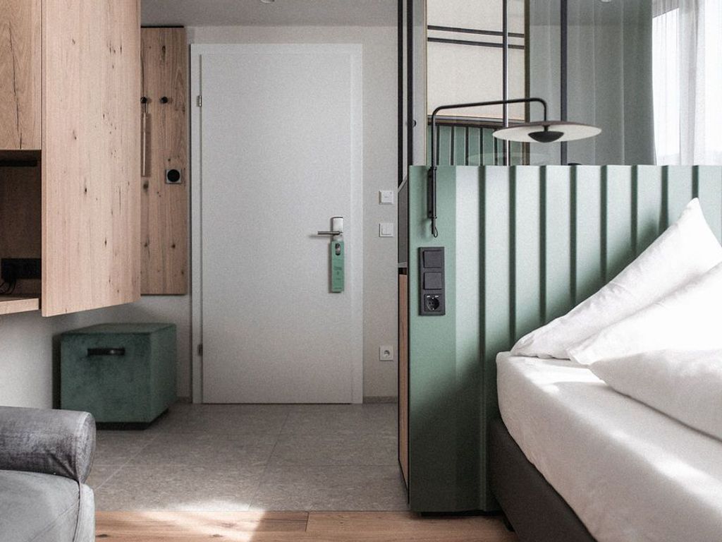 Ein Zimmer mit einem Bett, einem grünen Schrank, einem kleinen grünen Hocker und einer Tür.