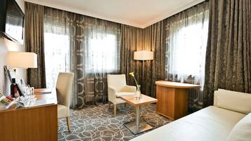 Ein Hotelzimmer mit Bett, Schreibtisch, Stuhl, einem kleinen Tisch mit Vase und zwei Lampen.