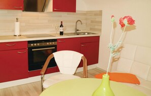 A modern kitchen with red cabinets, a stove, and a sink. There is a white chair and a green table with a vase. - Pet friendly apartment in Schleusingen (Schleusingen)