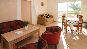 Ein Wohnzimmer mit einer Couch, Sesseln, einem Couchtisch und einem Esstisch mit Stühlen. Eine Tür, ein Fenster mit Blick und ein kleiner Tisch mit einer Pflanze sind ebenfalls vorhanden.