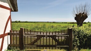 Une porte en bois avec un loquet métallique, un bâtiment blanc agrémenté de touches de rouge, et un champ avec un arbre en arrière-plan.