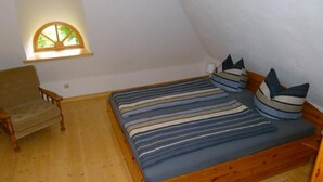 A small, cozy room with a wooden bed, a chair, and a window with a view of greenery. - Apartment (DG) - Old rectory Rappin (Rappin)