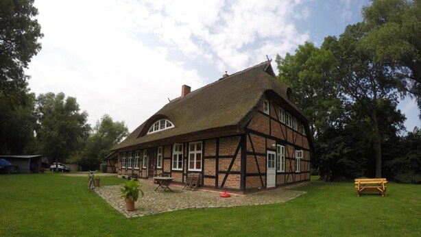 A traditional half-timbered house with a thatched roof, a small garden with a lawn, and a wooden bench. - Apartment (DG) - Old rectory Rappin (Rappin)