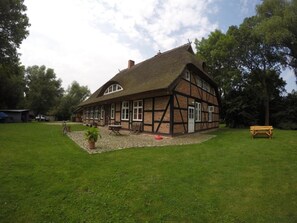 Une maison traditionnelle à colombages, avec un toit de chaume, une cour pavée et un banc.