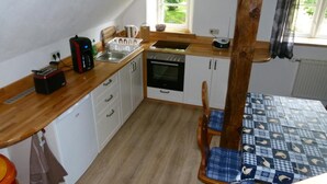 A compact kitchen with a wooden countertop, a coffee maker, a kettle, and a sink. There is a dining table with a checkered tablecloth and two chairs. - Apartment (DG) - Old rectory Rappin (Rappin)