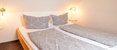 A neatly made bed with a geometric-patterned bedspread and pillows, two wall-mounted reading lamps, and a small bedside table.