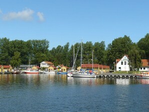 A marina with boats docked, a white building with a red roof, and a forested background.