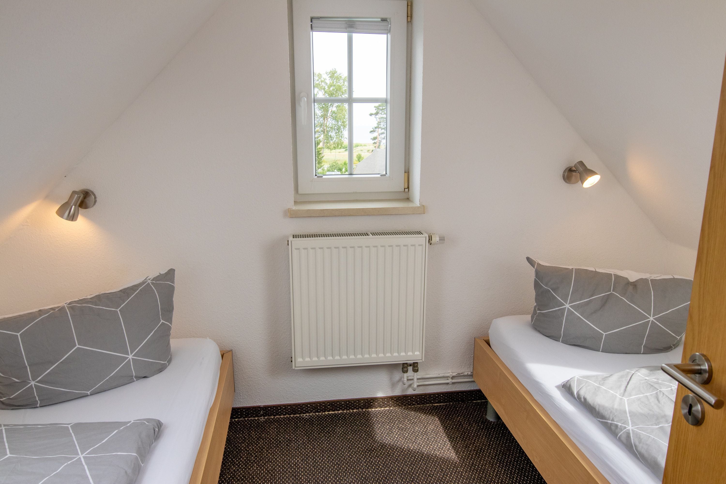 Una habitación pequeña con dos camas, una ventana, un radiador y una puerta.