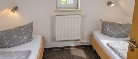Una habitación pequeña con dos camas, una ventana, un radiador y una puerta.