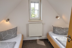 A small room with two beds, a window, a radiator, and a door. - Apartment 2 - Apartments in Blu Hus (Kröslin)
