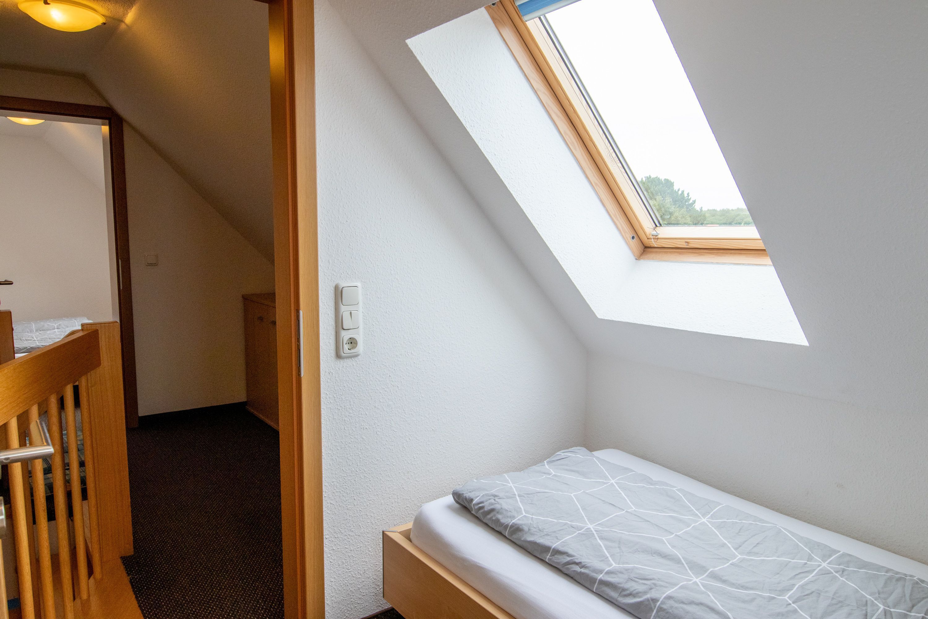 Une petite chambre avec un lit simple, un plafond en pente et un puits de lumière.