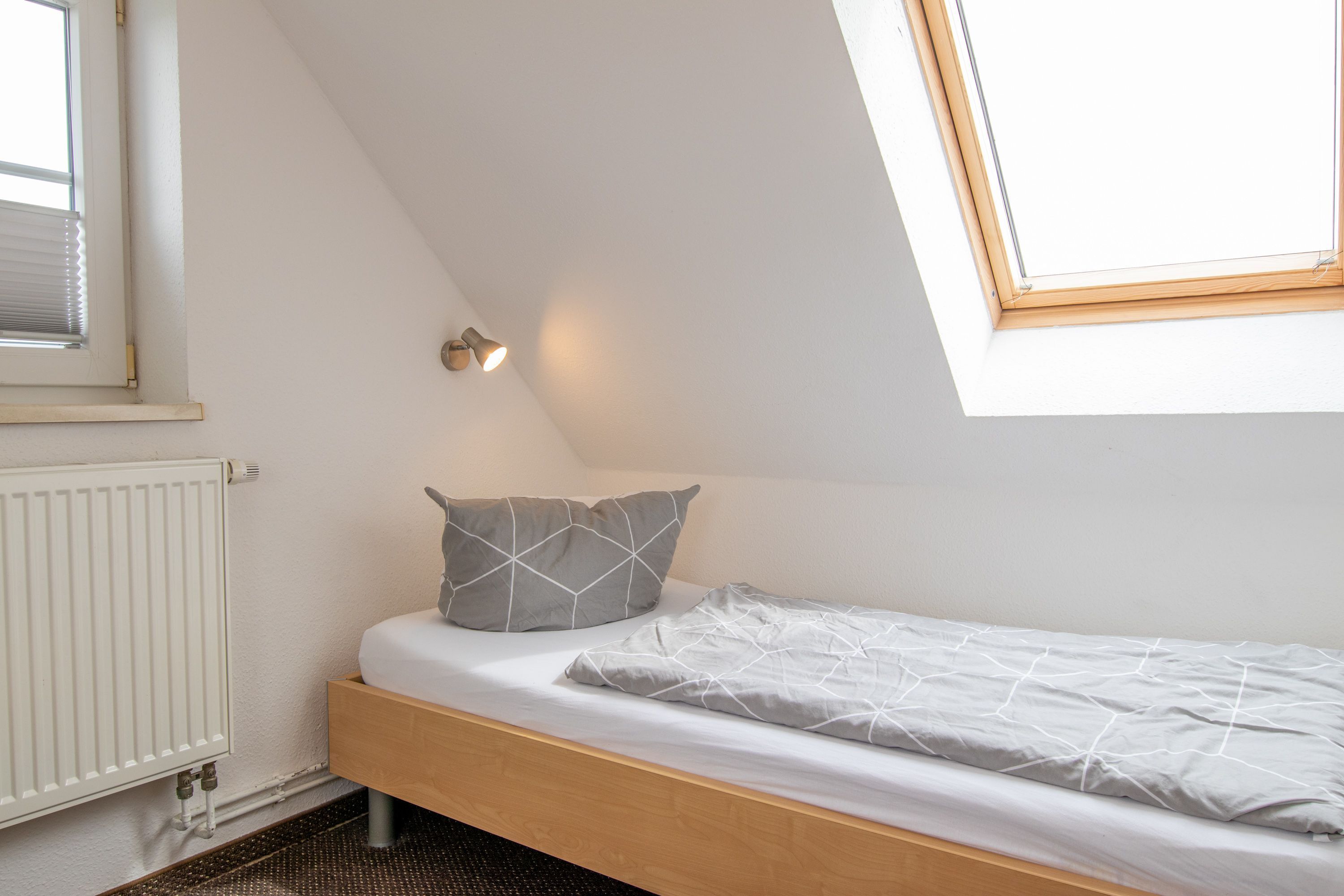 Un lit simple avec un cadre en bois, un matelas blanc et deux oreillers à motifs géométriques.