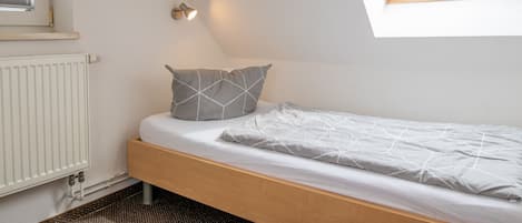 Un lit simple avec un cadre en bois, un matelas blanc et deux oreillers à motifs géométriques.
