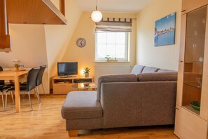 A cozy living area with a sofa, a TV, a dining table with chairs, a window with a view, and a cabinet with glass doors.