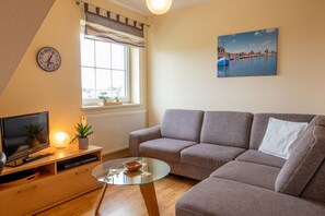A modern living room with a sofa, a glass coffee table, a television, and a clock on the wall.