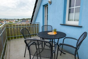 A blue building with a balcony, a round table with chairs, and a potted plant.