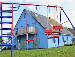 A playground with swings and a climbing structure in front of a blue house. - Apartment 2 - Apartments in Blu Hus (Kröslin)