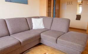 A sectional sofa with a white pillow, a glass coffee table, and a wooden floor. - Apartment 2 - Apartments in Blu Hus (Kröslin)