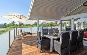 Een overdekt terras buiten met een tafel en stoelen, omringd door glazen hekwerk en parasols.
