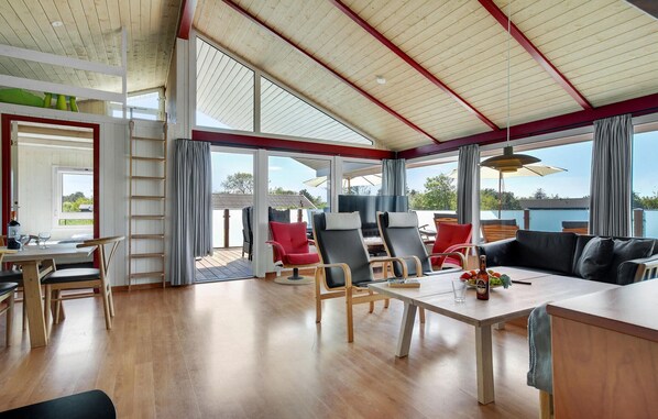Een ruime kamer met houten vloer, een zithoek met tafel en stoelen, een bank en een groot raam met uitzicht op de omgeving.