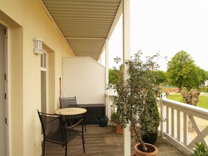 Een overdekt terras met een tafel, stoelen, een bloempot en uitzicht op de omgeving.