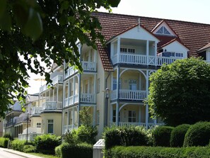 Een rij meerverdiepingsgebouwen met balkons, een rooddak en een verzorgde tuin.
