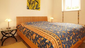 A bedroom with a bed, two bedside tables, a window with blinds, and a wall-mounted painting.