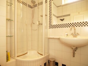 Een badkamer met een glazen douchecabine, een wastafel met spiegel en een betegelde muur met ruitpatroon.