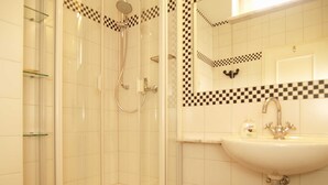 A bathroom with a glass-enclosed shower, a sink with a mirror, and a checkered tile backsplash.