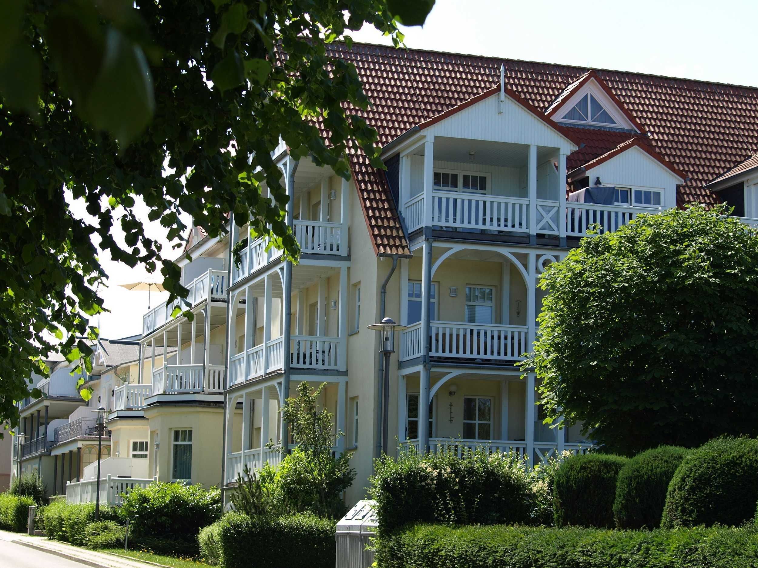 A row of multi-story buildings with balconies, a red-tiled roof, and a well-maintained garden.