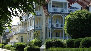 A row of multi-story buildings with balconies, a red-tiled roof, and a well-maintained garden.