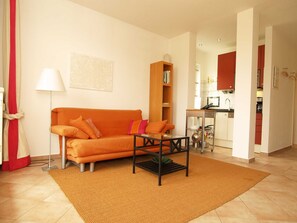 Een woonkamer met een oranje bank, een bijzettafeltje en een boekenkast.