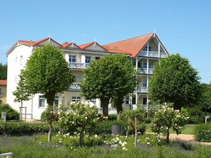 Een meerhoog gebouw met een rode pannendak, witte balkons en weelderige begroeiing op de voorgrond.