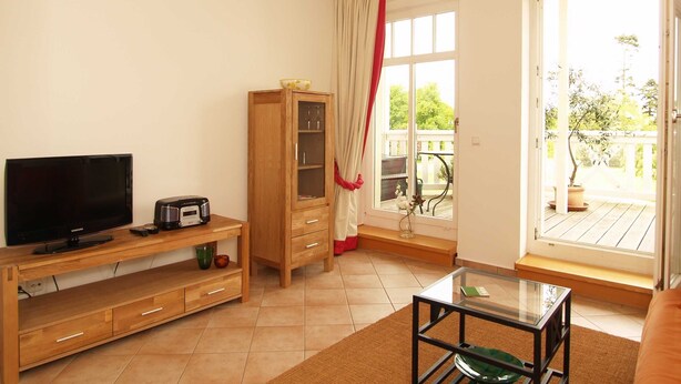 A living room with a TV, radio, wooden cabinet, glass table, and a view of the outdoors through a large window.