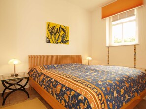 Een slaapkamer met een bed, twee nachtkastjes, een raam met zonwering en een aan de muur hangend schilderij.