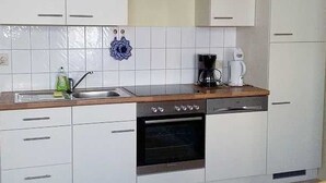 Een keuken met witte kastjes, een roestvrijstalen spoelbak, een koffiezetapparaat en een inbouwoven.