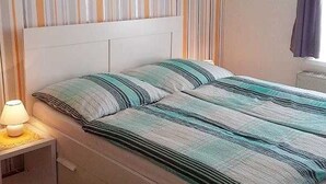 Een bed met een gestreept laken, een bedlampje en een gestreepte gordijn.