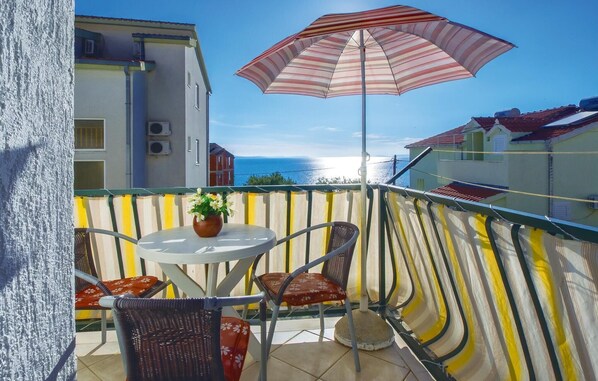 A balcony with a table, chairs, a striped umbrella, and a view of the sea. - Stunning apartment in Omis with WiFi (Omis)