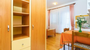 A room with a wooden wardrobe, a dining table with chairs, and a window with curtains.