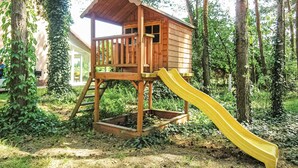 Una casita de juegos de madera con un tobogán en un área boscosa.