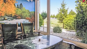 Una habitación con puerta de vidrio que da a un jardín, una mesa redonda con sillas y un mural con un paisaje de bosque.